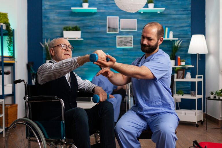 Senior man in wheelchair exercises with dumbbells, assisted by a caregiver.