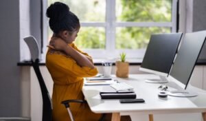 Woman experiencing neck pain at an ergonomic workstation